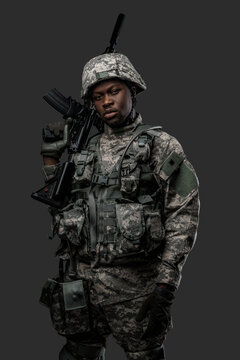Photo of handsome military man of african ethnic armed with rifle isolated on gray.