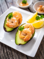 Avocado with fried prawns on and cocktail sauce on wooden background