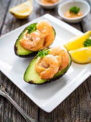 Avocado with fried prawns on and cocktail sauce on wooden background