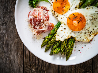 Sunny side up eggs with green asparagus  fried bacon on black plate on wooden table
