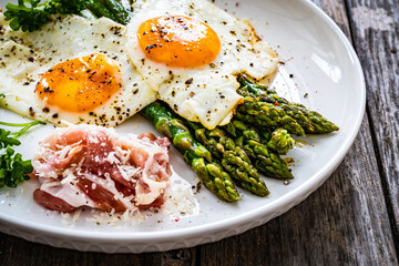 Sunny side up eggs with green asparagus  fried bacon on black plate on wooden table
