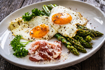Sunny side up eggs with green asparagus  fried bacon on black plate on wooden table
