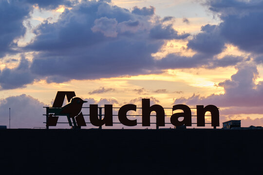 Auchan logo sign above store, with sunset clouds. Auchan is a French multinational retail group owned by the Mulliez family. Bucharest, Romania - May 26, 2022.