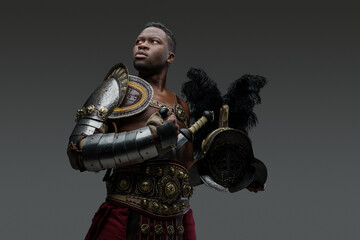 Portrait of ancient roman gladiator of african descent dressed in light armor holding plumed helmet.
