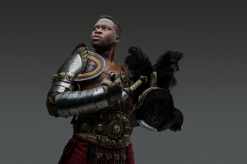 Fototapeta premium Portrait of ancient roman gladiator of african descent dressed in light armor holding plumed helmet.