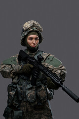 Studio shot of military woman dressed in camouflage clothes and helmet holding rifle.