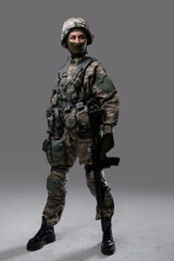 Photo of isolated on gray special forces woman holding rifle dressed in uniform with helmet.