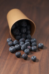 Ripe blueberries spilling from paper cup on wood table