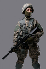 Photo of isolated on gray special forces woman holding rifle dressed in uniform with helmet.