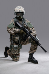 Portrait of soldier woman with rifle sitting on her knee isolated on grey background.