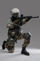 Studio shot of militant woman dressed in protective suit aiming rifle looking away.