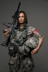 Photo of brown haired female soldier dressed in camouflage uniform holding rifle on her shoulder.