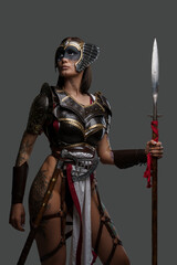 Portrait of ancient amazon with spear dressed in armour against grey background. - obrazy, fototapety, plakaty