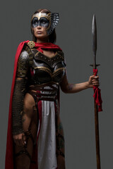 Studio shot of ancient woman soldier dressed in steel armor with cape holding spear.