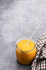 Yellow and orange fruit puree in glass jar on gray background