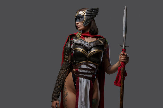 Studio shot of wild female warrior from past with painted face holding spear isolated on grey background.