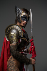 Shot of female warrior with painted face dressed in armor and red cape against grey background.