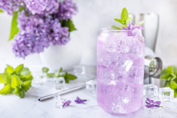 Obraz na płótnie Canvas Lilac drink, infused drink from lilac flowers. Organic natural daikiri cocktail or mocktail, lilac lemonade with ice on a marble table.