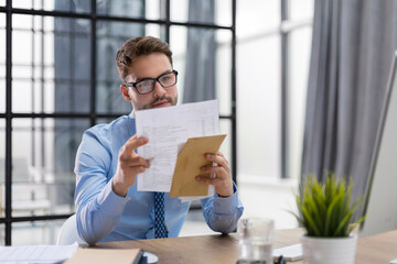 Handsome entrepreneur reading a letter from envelope in a desktop at office.