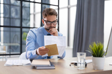 Handsome entrepreneur reading a letter from envelope in a desktop at office.