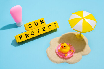 Summer skin care concept. Sunscreen, duck in inflatable ring , sand and sun umbrella on a blue...