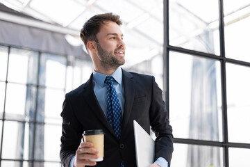 Businessman walking in office corridor with takeaway coffee.