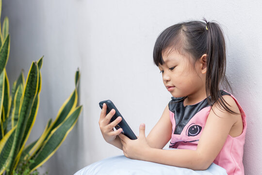 Portrait image of 4-5 years old childhood. Happy Asian child girl watching and using smart phone. She laying on the bed or sofa in rest room. Leaning and using technology , social media concept.