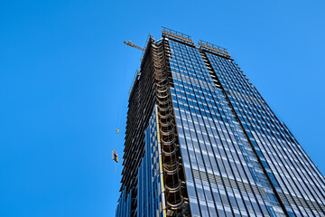 A yellow hook of a tower crane lifts the window load along skyscraper under construction against...