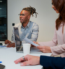 Young African American boy talking in a work meeting with a Caucasian girl and another unrecognizable man.