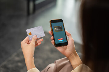 Beautiful businesswoman payment by credit card on mobile phone for online shopping, copy space at background, selective focus at credit card. Young woman shopping online in home office