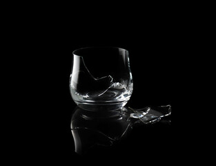 Broken empty whiskey glass isolated on black background.
