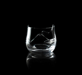 Broken empty whiskey glass isolated on black background.