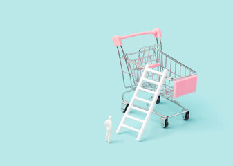 Shopping cart with ladder and man figurine standing below. Rising costs, inflation conceptual...
