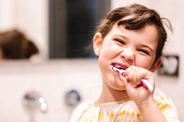 elementary girl smiles as she looks at the camera cleaning her teeth