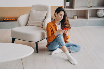 Obraz premium Caucasian young woman enjoying music in headphones. Girl is sitting on floor at home.