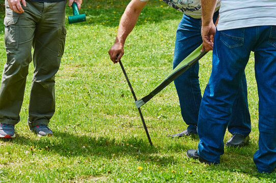 Men set up a large camping tent on the grass. Installation of a metal pin. The concept of outdoor recreation. The legs of men, part of the tent and a hammer in his hand. Sunny day. Selective focus.