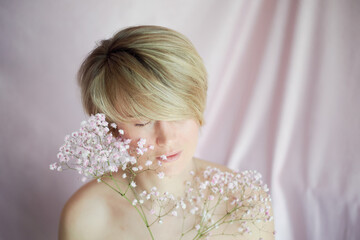 Portrait of a girl on a pink background with flowers. Tenderness and feminine. The sphere of beauty and women's health. Short haircut, blonde hair