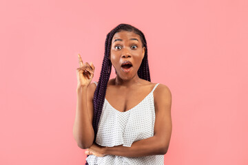 Surprised young black lady in summer outfit pointing upwards, having creative idea on pink studio...