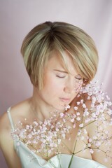 Portrait of a girl on a pink background with flowers. Tenderness and feminine. The sphere of beauty and women's health. Short haircut, blonde hair