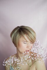 Portrait of a girl on a pink background with flowers. Tenderness and feminine. The sphere of beauty and women's health. Short haircut, blonde hair