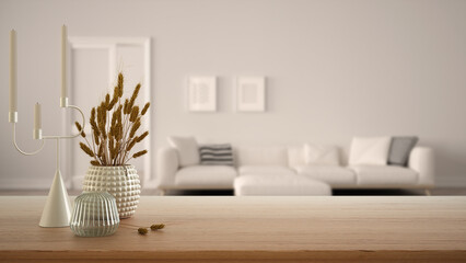Wooden table, desk or shelf close up with ceramic and glass vases with dry plants, straws over blurred view of white living room with sofa and door, modern interior design concept