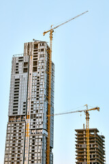 White and blue glass skyscraper under construction with a yellow tower crane along it and a smaller...