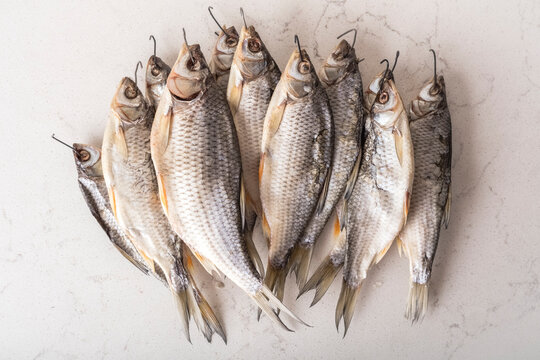 A set of dried fish with hooks for drying on a rope. Roach on a white table