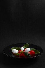 caprese salad in black plate on black background with copy space