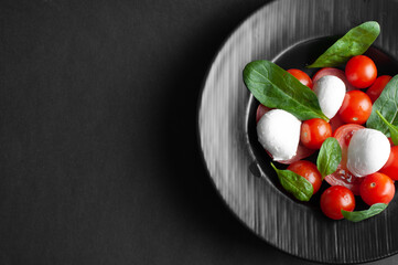 top view of half black plate with caprese salad on black background with copy space