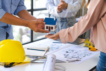 Construction and structure concept of Engineer or architect holding a model of house wood to present and give to the customer,  the contract between the two companies' real estate concept