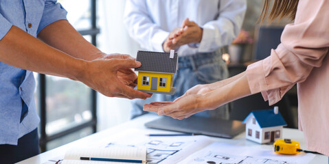 Construction and structure concept of Engineer or architect holding a model of house wood to present and give to the customer,  the contract between the two companies' real estate concept