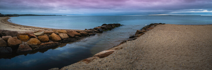 Dramatic cloudy seascape with the river flowing into the sea through the jetty banks on the beach on Cape Cod, Massachusetts