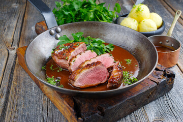 Traditionell gegrilltes Gourmet Entenbrust Filet mit Haut serviert mit Kartoffelknödel in Dunkelbier Sauce als Draufsicht in einer rustikalen Bratpfanne