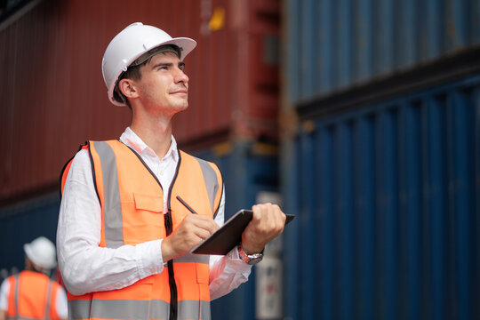 Dock manager or engineer worker in safety vest standing in shipping container yard holding tablet with smile. Import and export product. Manufacturing transportation and global business concept.